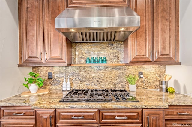 kitchen featuring tasteful backsplash, light stone counters, wall chimney range hood, and stainless steel gas cooktop