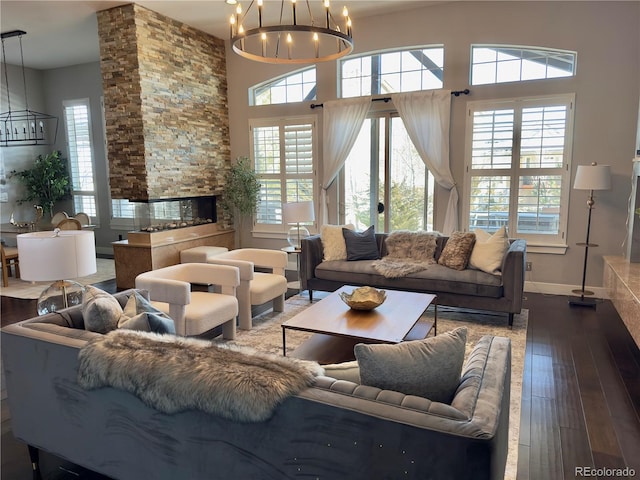 living room featuring hardwood / wood-style flooring, a stone fireplace, a chandelier, and a towering ceiling