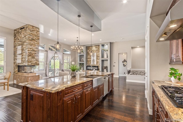 kitchen featuring a large island, sink, range hood, a fireplace, and decorative light fixtures