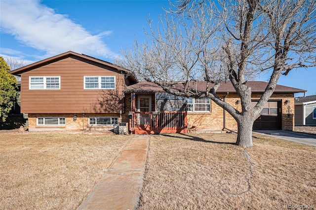 split level home featuring a garage, a front lawn, concrete driveway, and brick siding