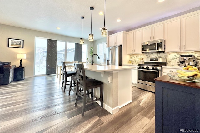 kitchen with stainless steel appliances, tasteful backsplash, hanging light fixtures, and a kitchen island with sink