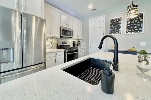 kitchen featuring appliances with stainless steel finishes, pendant lighting, tasteful backsplash, white cabinetry, and sink