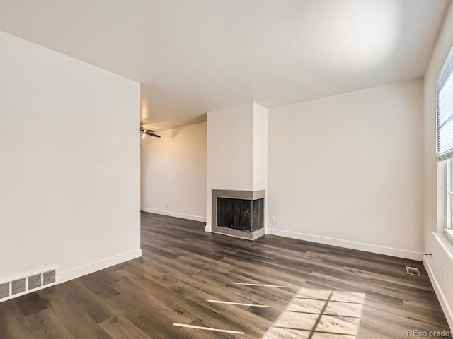 unfurnished living room with dark wood-style flooring, a multi sided fireplace, visible vents, and baseboards