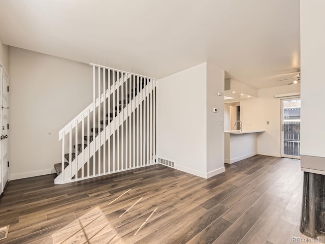 unfurnished living room with visible vents, stairway, a sink, wood finished floors, and baseboards