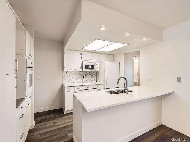 kitchen featuring a peninsula, white appliances, a sink, decorative backsplash, and dark wood finished floors