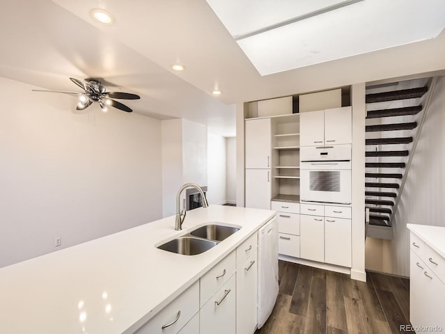 kitchen with white cabinets, dark wood finished floors, white oven, light countertops, and a sink