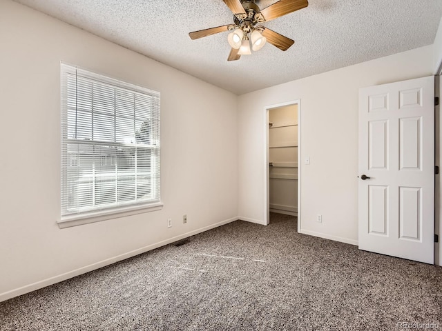 unfurnished bedroom with a textured ceiling, a ceiling fan, baseboards, carpet, and a walk in closet