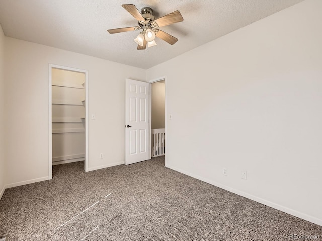 unfurnished bedroom with carpet, a walk in closet, ceiling fan, a textured ceiling, and baseboards