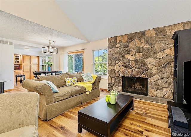 2650 S Vaughn Way Unit B, Aurora, CO 80014 - living room featuring a stone fireplace, light wood finished floors, a chandelier, lofted ceiling, and a textured ceiling