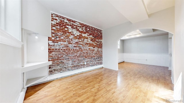 empty room featuring a wainscoted wall, brick wall, arched walkways, and wood finished floors