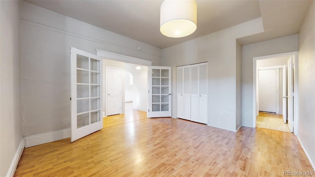 spare room featuring french doors, baseboards, and light wood finished floors