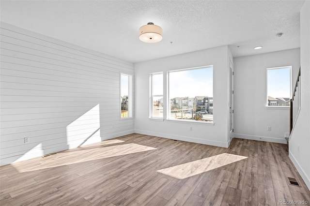 empty room featuring a wealth of natural light, a textured ceiling, and light hardwood / wood-style floors