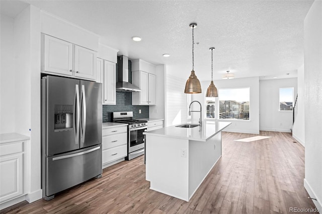 kitchen featuring wall chimney exhaust hood, sink, white cabinetry, a center island with sink, and appliances with stainless steel finishes