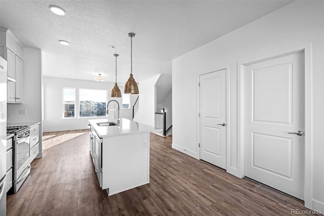 kitchen with stainless steel range oven, sink, a center island with sink, pendant lighting, and white cabinets