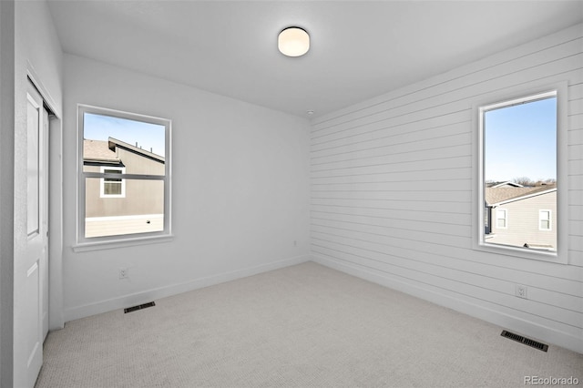 spare room with light colored carpet and wood walls