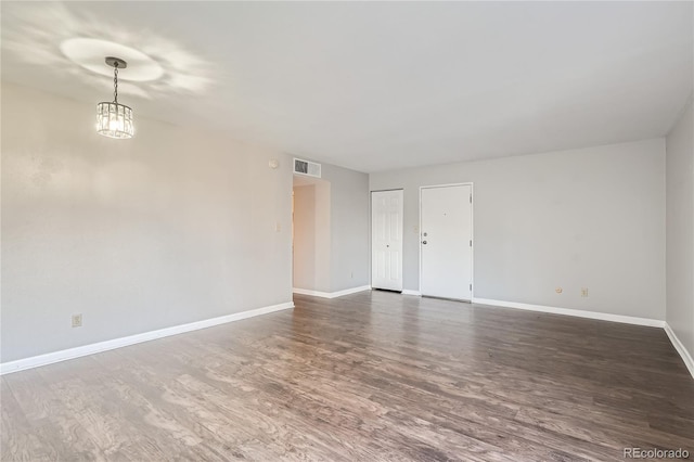 spare room featuring dark hardwood / wood-style flooring and a chandelier