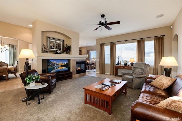 living room featuring ceiling fan with notable chandelier, carpet flooring, and a fireplace