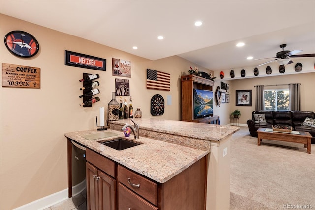 kitchen with light colored carpet, kitchen peninsula, light stone countertops, ceiling fan, and sink