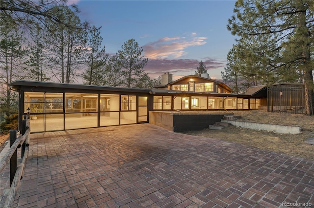 back house at dusk featuring a sunroom and a patio