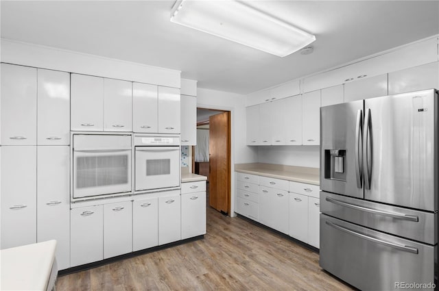 kitchen with light hardwood / wood-style flooring, stainless steel fridge, white oven, and white cabinets