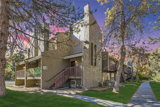 property exterior at dusk featuring stucco siding, a yard, and stairs