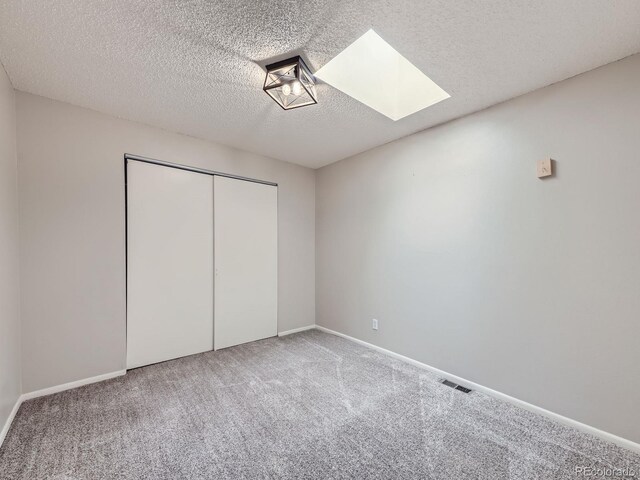 unfurnished bedroom featuring a textured ceiling, a skylight, visible vents, a closet, and carpet