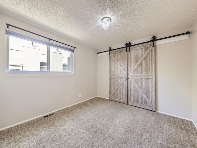 unfurnished bedroom with a barn door, carpet, visible vents, and baseboards