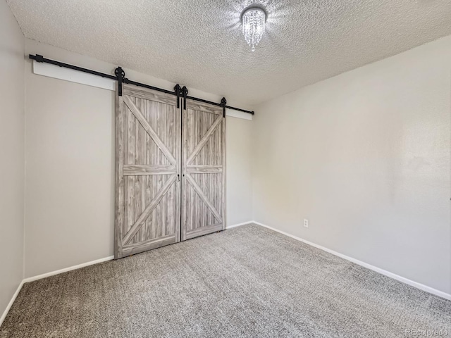 unfurnished bedroom featuring a textured ceiling, a barn door, carpet flooring, and baseboards