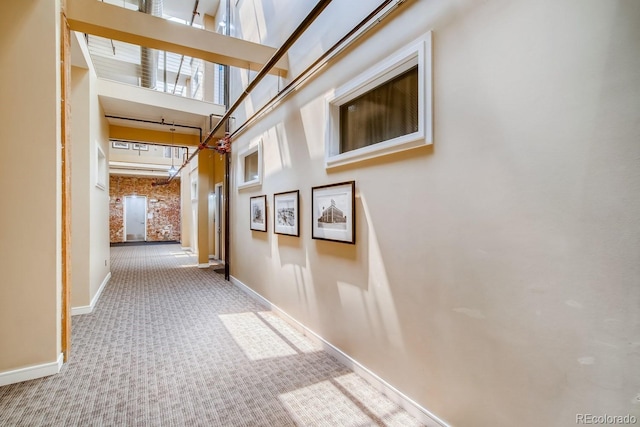 hall featuring carpet, brick wall, and a towering ceiling