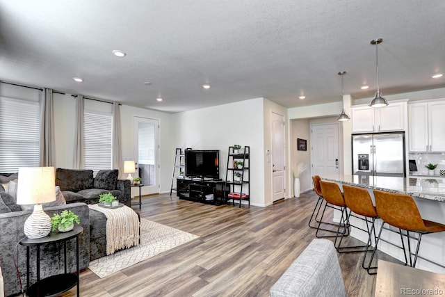 living area featuring a textured ceiling, baseboards, wood finished floors, and recessed lighting