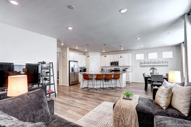 living area featuring baseboards, a textured ceiling, light wood-type flooring, and recessed lighting