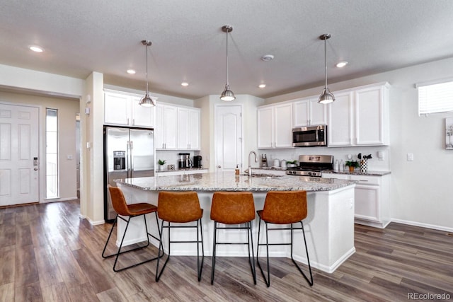 kitchen with dark wood-style floors, a center island with sink, appliances with stainless steel finishes, white cabinets, and a sink