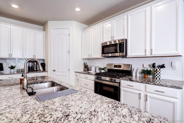 kitchen with backsplash, white cabinetry, stainless steel appliances, and a sink