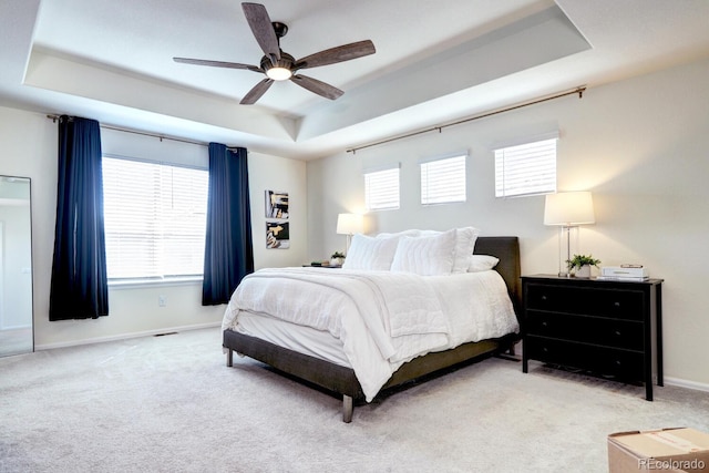 carpeted bedroom featuring a ceiling fan, a tray ceiling, and baseboards