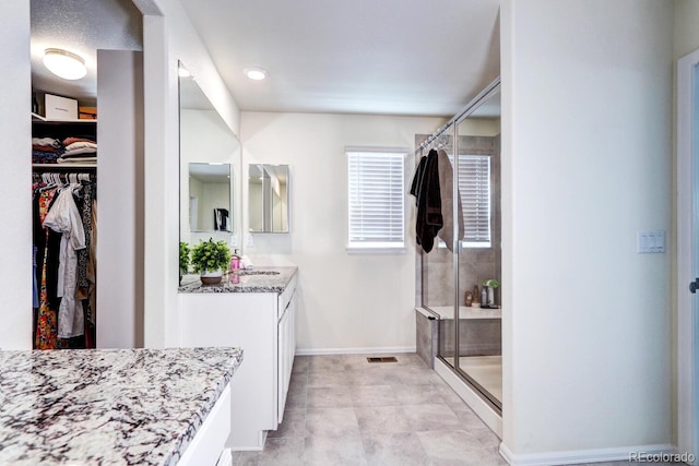 full bathroom with visible vents, vanity, baseboards, a shower stall, and a walk in closet