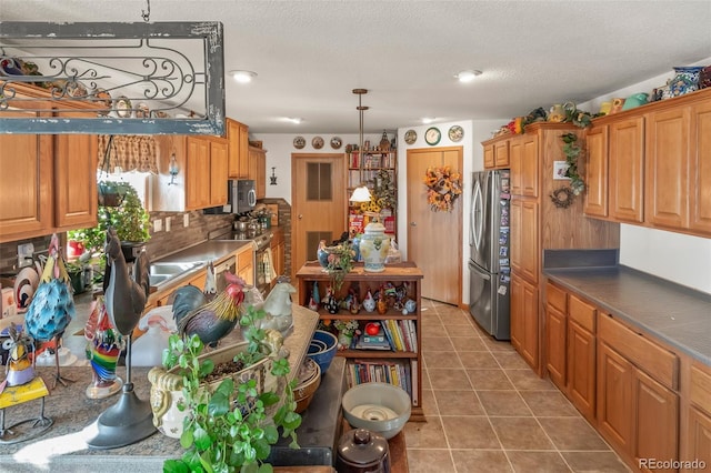 kitchen featuring pendant lighting, backsplash, tile patterned flooring, stainless steel appliances, and a textured ceiling