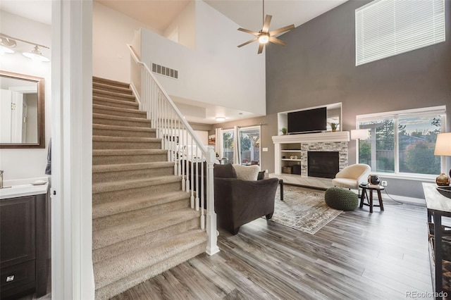 living room with ceiling fan, wood-type flooring, a high ceiling, and a fireplace