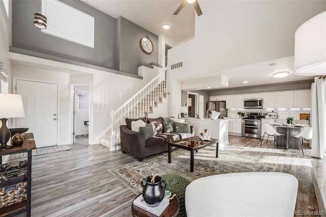 living room with light hardwood / wood-style floors, a towering ceiling, and ceiling fan