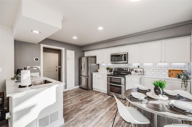 kitchen with decorative backsplash, light hardwood / wood-style flooring, sink, white cabinetry, and appliances with stainless steel finishes