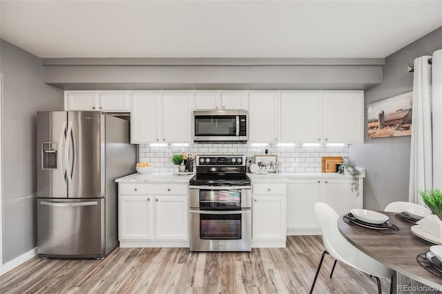 kitchen with backsplash, white cabinetry, stainless steel appliances, and light hardwood / wood-style floors