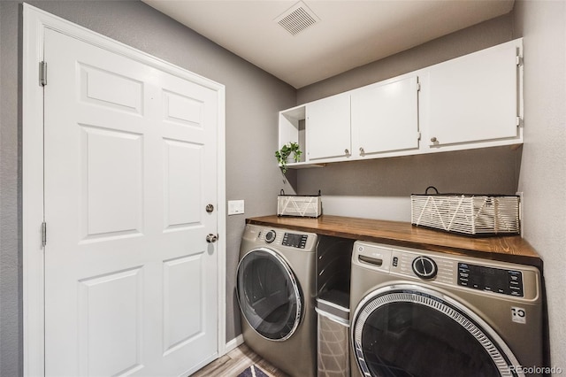 clothes washing area featuring washer and dryer, light hardwood / wood-style floors, and cabinets