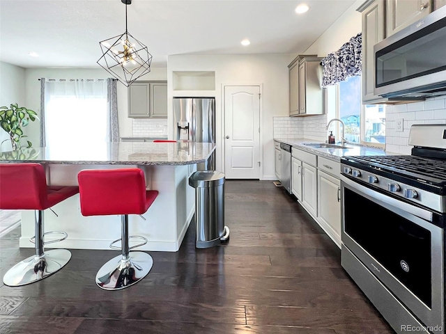 kitchen with a sink, appliances with stainless steel finishes, light stone countertops, dark wood-style floors, and a kitchen bar