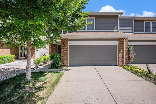 townhome / multi-family property with concrete driveway, brick siding, an attached garage, and roof with shingles