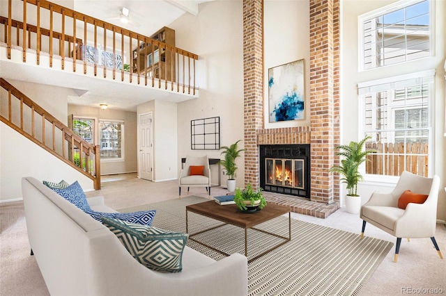carpeted living room with a fireplace, baseboards, a towering ceiling, ceiling fan, and stairs