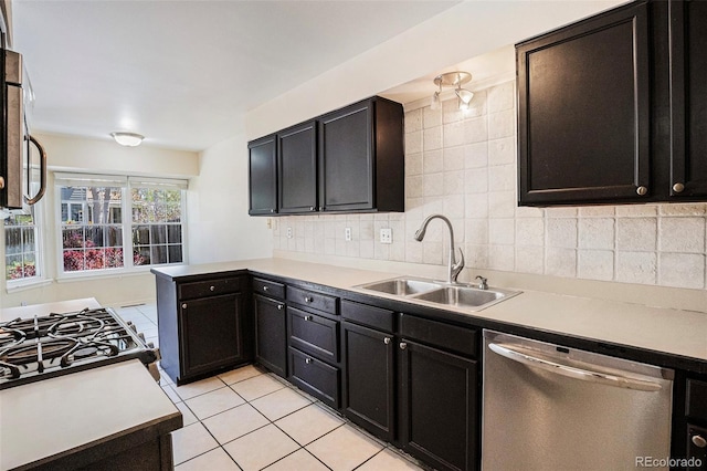 kitchen with appliances with stainless steel finishes, a sink, a peninsula, backsplash, and light tile patterned flooring