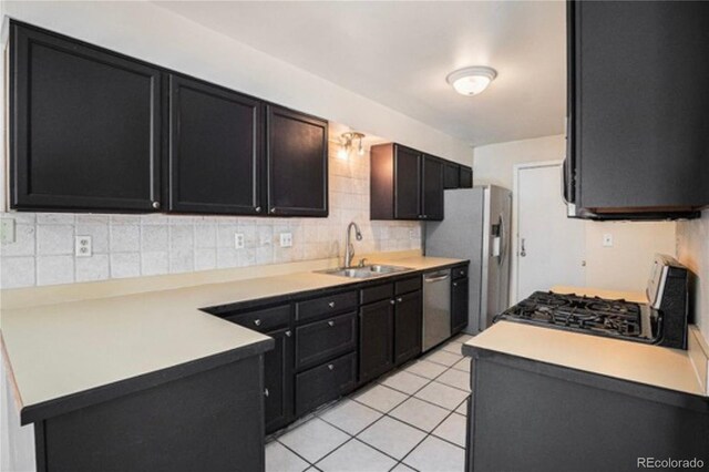 kitchen featuring stainless steel appliances, a sink, backsplash, a peninsula, and light countertops