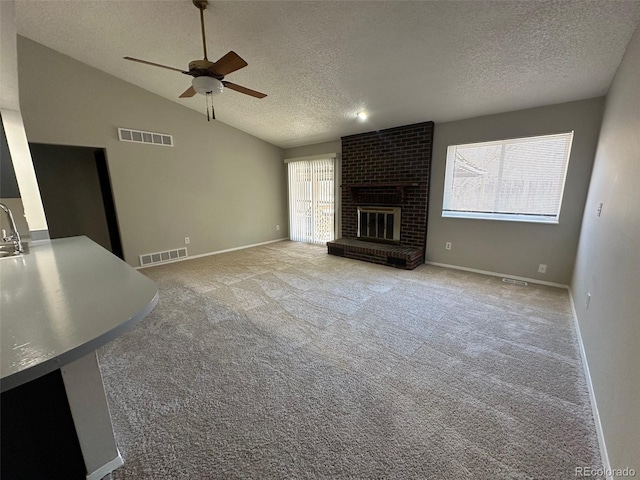 unfurnished living room with light carpet, a textured ceiling, vaulted ceiling, ceiling fan, and a fireplace