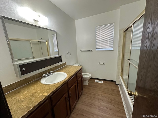 full bathroom featuring hardwood / wood-style floors, vanity, toilet, and bath / shower combo with glass door