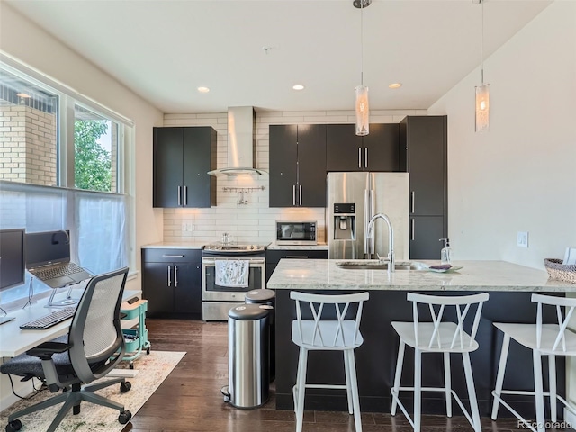 kitchen with appliances with stainless steel finishes, sink, a breakfast bar area, hanging light fixtures, and wall chimney range hood