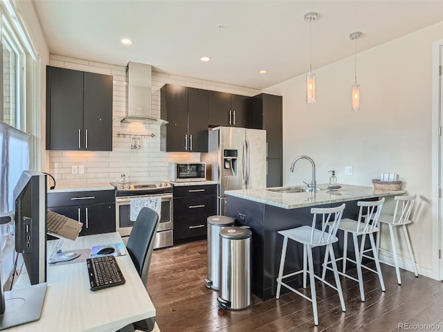 kitchen with a kitchen breakfast bar, hanging light fixtures, stainless steel appliances, light stone countertops, and wall chimney exhaust hood